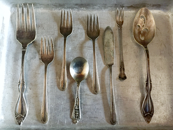 Silverware placed in single layer in an aluminum pan for cleaning.