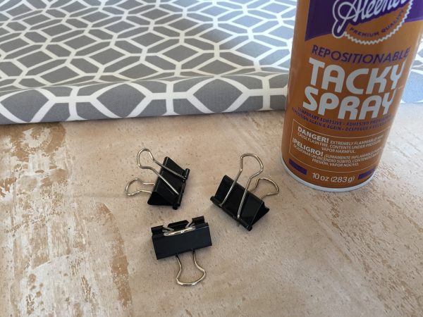 Items needed to decorate the back of a shelving unit: Fabric, tacky spray, and clips