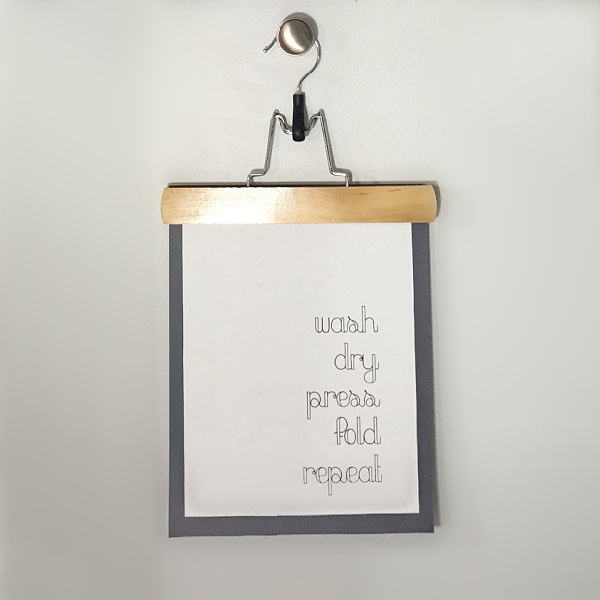 Laundry printable clipped with a wooden pants hanger hung on a knob