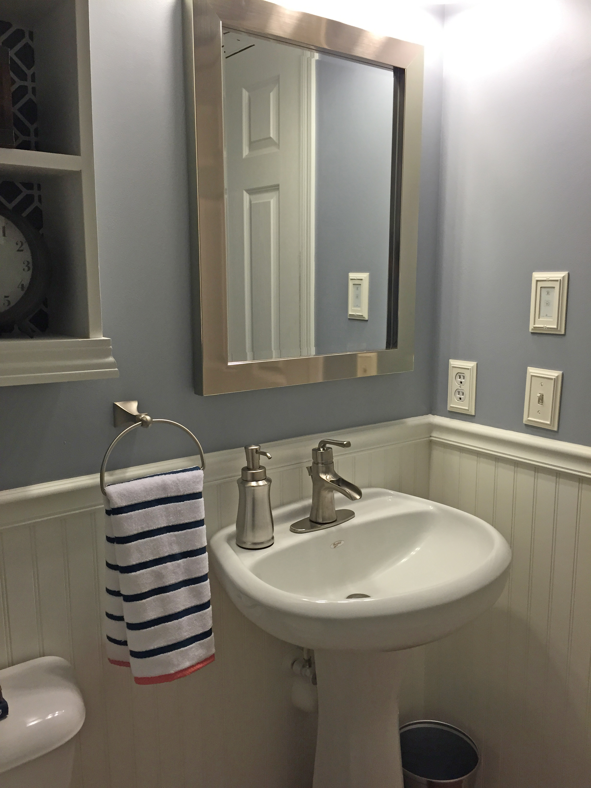 Powder Room Makeover with view of pedestal sink with new faucet, new mirror, and towel holder with stripped towel
