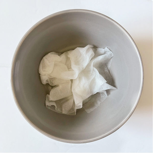 Small bowl with vinegar soaked paper towels used to remove hard water stains from faucets