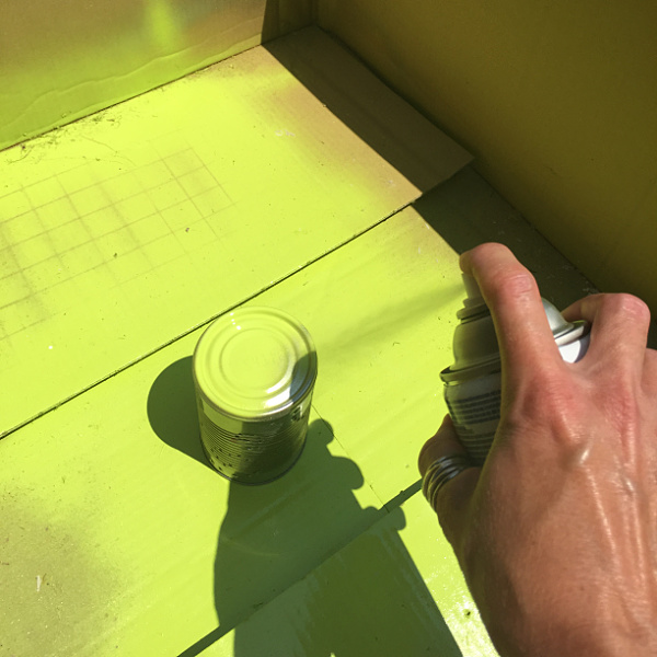 Spray painting a tin can with lime green spray paint