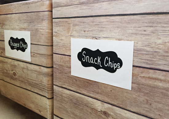 Boxes wrapped in wood-print paper, labeled with a chalkboard stick. Used for pantry organization