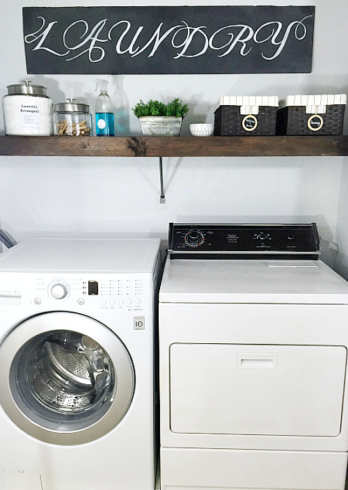 Laundry room after $100 room makeover featuring a painted dryer, DIY wood overlay to cover wire shelving, and a chalkboard sign made from cardboard