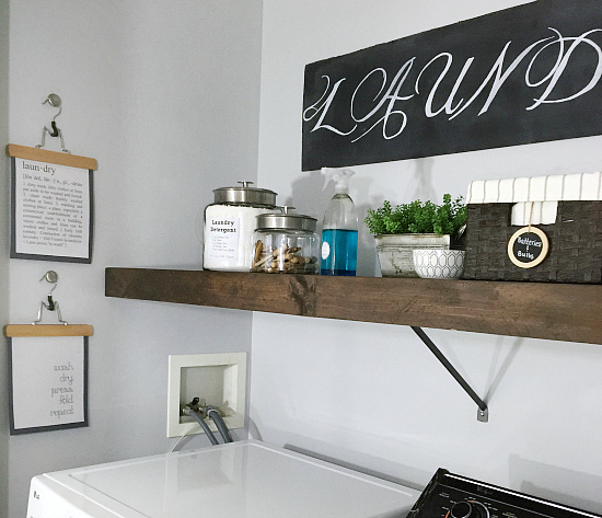 $85 Laundry room makeover includes a wood shelf overlay to cover the wire shelving, free printable hung from pants hangers, and a large chalkboard sign made from cardboard