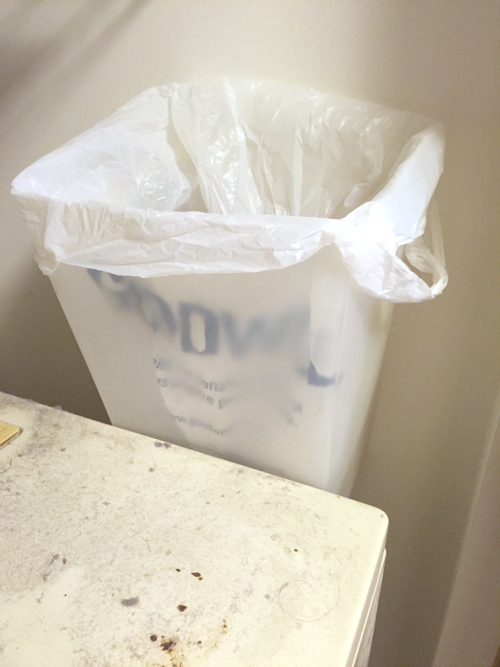 Trash can shoved between dryer and wall for lint disposal