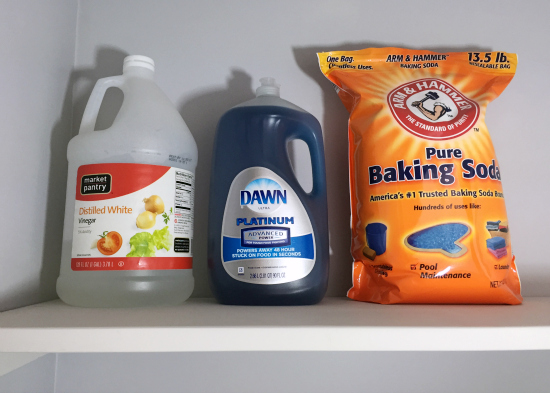 White wood shelf in cleaning closet holding various cleaning items: Vinegar, dish soap, and baking soda