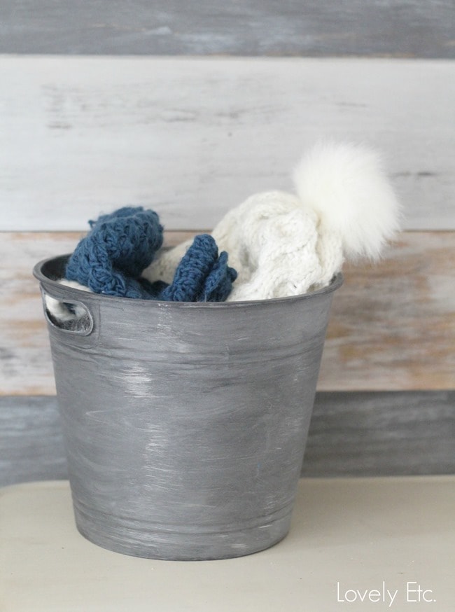 Dollar store bin after makeover with paint, being used to hold hats and mittens