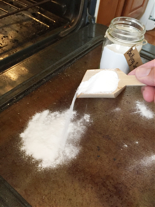 Sprinkling baking soda on glass oven door to clean