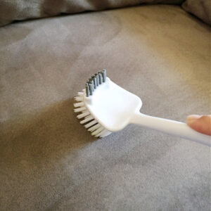 Using a soft bristle brush to loosen fibers after cleaning a microfiber couch