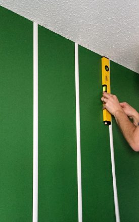 Using a level to adhere white trim strips to wall in order to create a football field wall