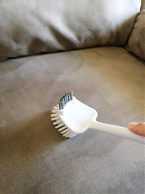 Using a soft bristle brush to loosen fibers after cleaning a microfiber couch