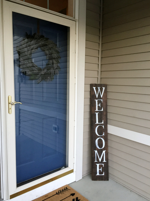 Barn wood welcome sign leaning in corner next to newly painted front door