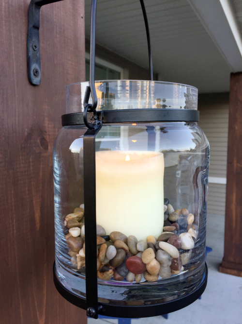 Glass lanterns hanging from metal hooks on newly stained pillar of porch