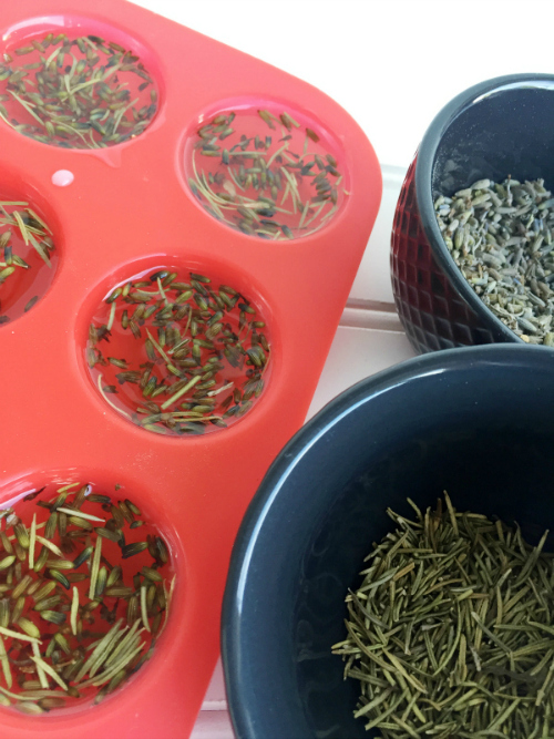 Sprinkling dried lavender and rosemary on top of melted wax to make DIY Wax Melts