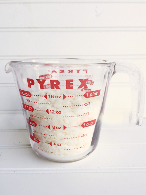 Glass measuring cup filled with soy wax flakes which will be used to make homemade wax melts for a wax warmer