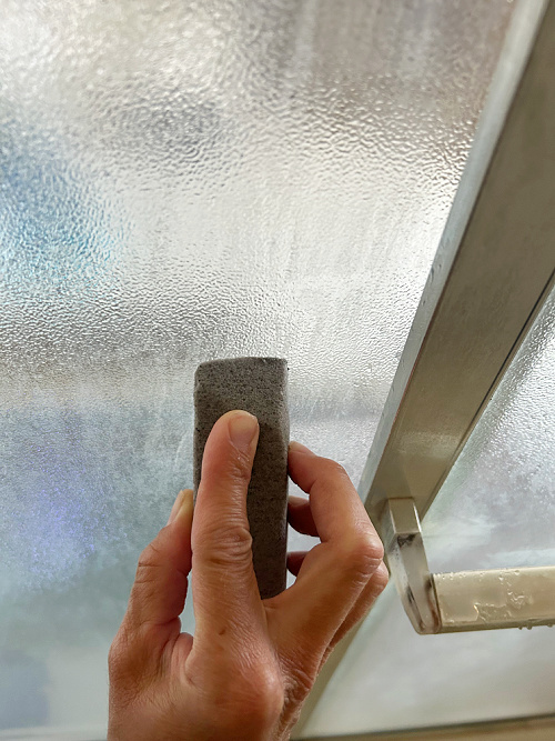 Scrubbing soap scum on glass shower door with pumice stone