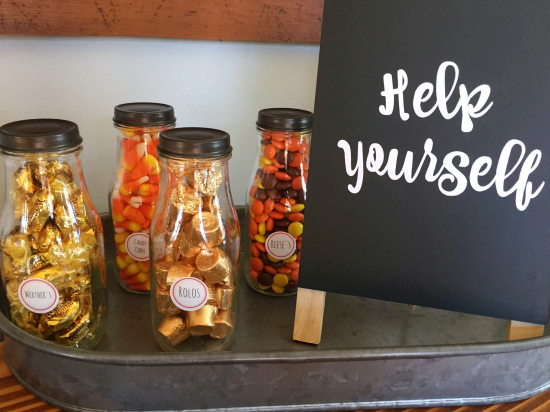 Various Halloween candies in small milk jars with a chalkboard sign that says "Help Yourself"