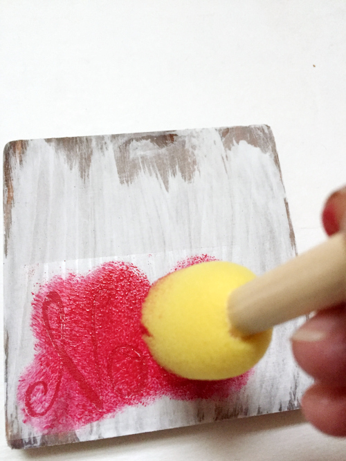 Using a round sponge brush to apply red paint to stencil