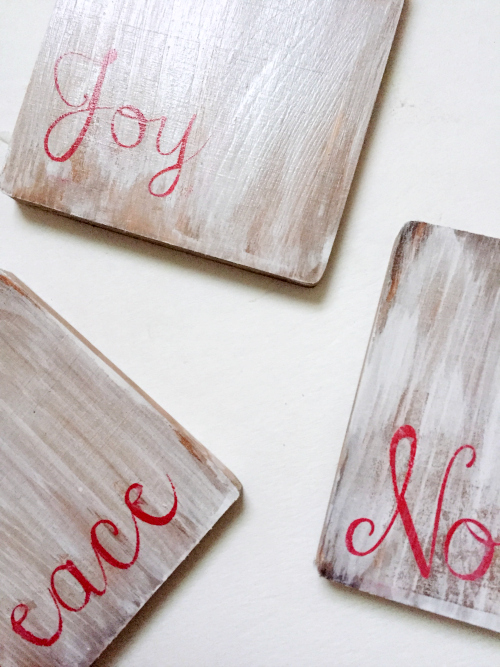 Finished white washed wooden coasters with the words joy, noel, and peace stenciled on them