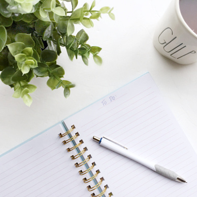Small open notebook with a pen on a desk next to a plant and coffee