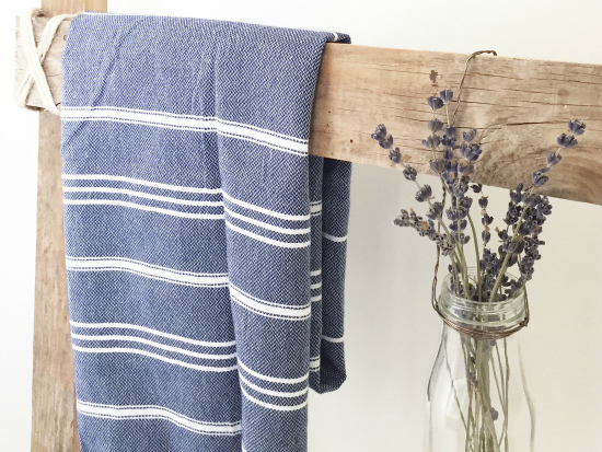 Rustic barnwood ladder with a blue Turkish towel and milk jar with dried lavender hanging from it.