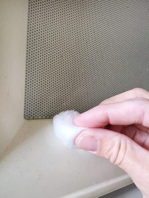 Wiping off grease on a microwave door using a cotton ball with lemon essential oil