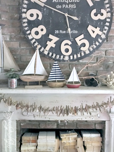 Fireplace mantel decorated for summer featuring a large clock and wooden sailboats