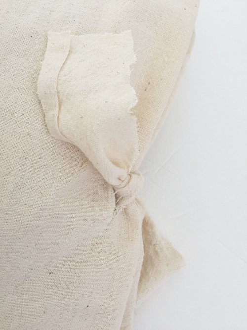 Fabric strip tied through front and back of DIY Farmhouse Pillow Cover as a closure