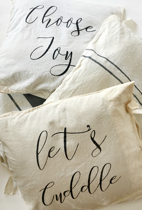 Stack of throw pillows displaying DIY Farmhouse Pillow Covers with both phrases and ticking stripes