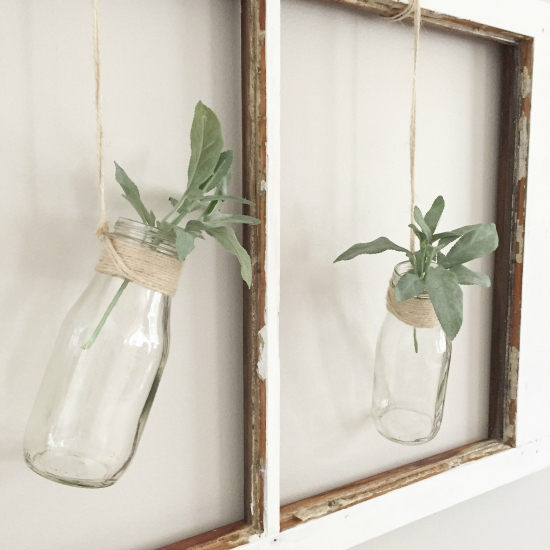 Old chippy window with milk jars hanging from twine with sprigs of greenery