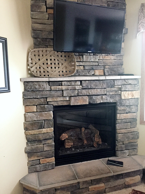 Stone fireplace with a tobacco basket on the mantel and a television above it