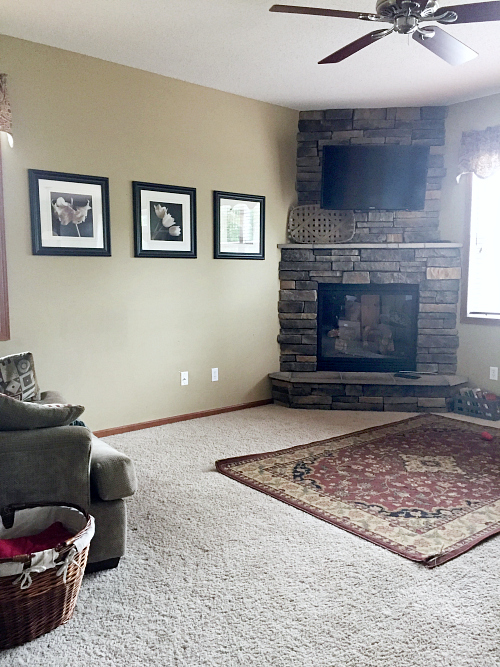 Outdated living room with beige walls, a corner fireplace, and a maroon oriental rug