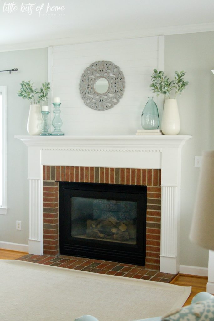 White fireplace decorated for summer featuring large cream vases with greenery and blue glass vases and candlesticks