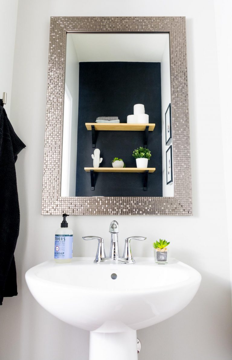 Powder room after a $100 makeover featuring a glitzy mirror and black accent wall with light wood floating shelving