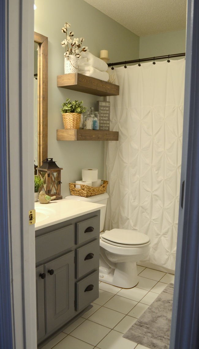 Bathroom after $100 makeover featuring newly painted walls and vanity with ruffled shower curtain and DIY floating wood shelves above the toilet