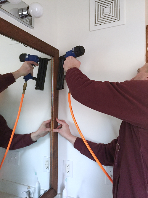 Using a nail gun to attach DIY frame to bathroom mirror