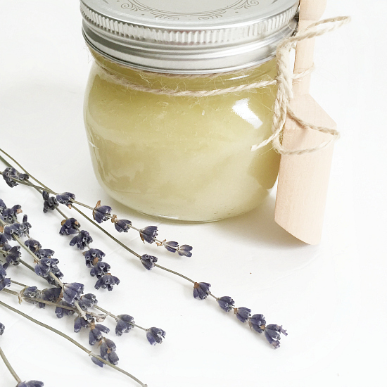 Homemade lavender sugar scrub in glass jar with a small wooden scoop attached with twine