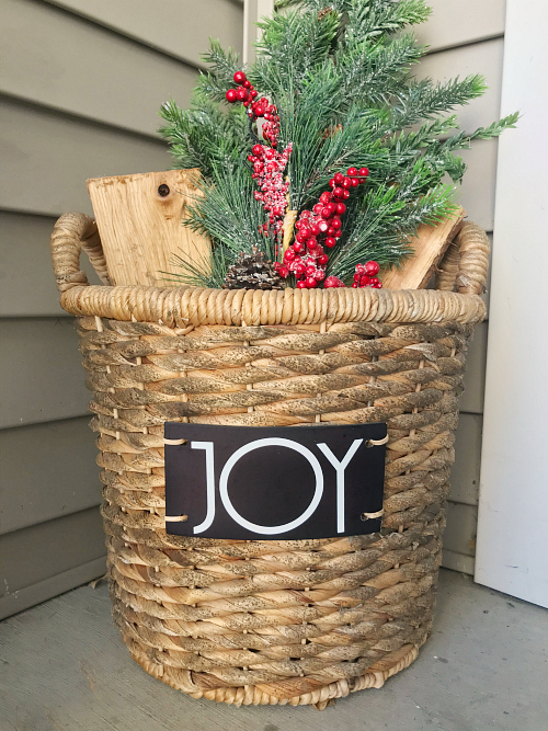 Basket filled with wood, faux pine and berries with the word Joy on chalkboard label.