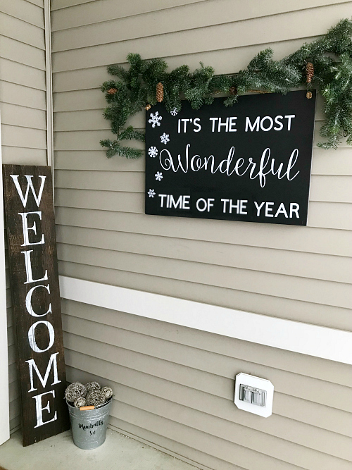 DIY Christmas sign hung on porch with garland above it