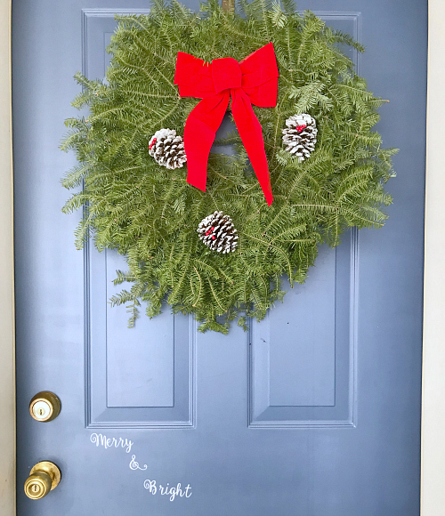 Traditional Christmas wreath hung on blue front door with the words 