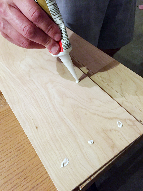 Applying liquid nails to underlayment in order to adhere the underlayment strips to a bifold door to make it look like a barn door