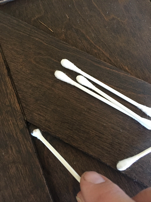 Using cotton swabs to apply stain in crevices of a faux barn door created from a bifold door