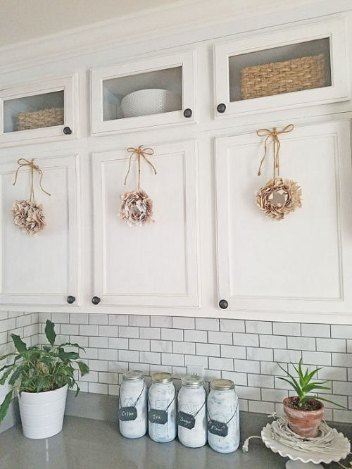 Book pages made into small wreaths and hanging from kitchen cabinets