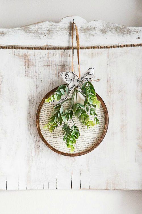 Book pages used as the background of an embroidery hoop with faux greenery attached.