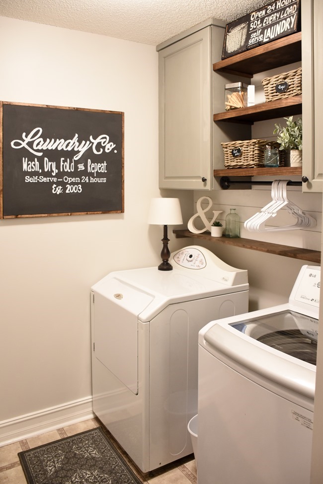 Laundry Room after $100 makeover. Displays newly painted cabinets and open wood shelving with a chalkboard sign.