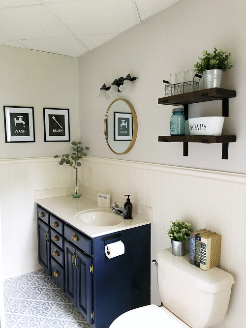 Classic farmhouse bathroom with navy vanity, stenciled floor, DIY wall decor, and DIY chunky wood shelves