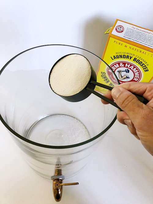 Pouring washing soda into a drink dispenser to make DIY Thieves Laundry Detergent