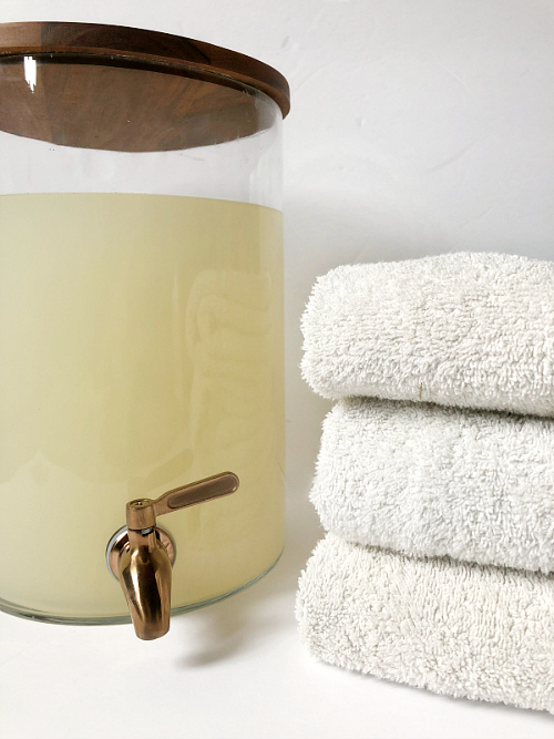 DIY Thieves Laundry Soap in a drink dispenser with folded white towels to the right. The DIY Thieves Laundry Detergent is free of harsh chemicals and costs less than $4/gallon. It's easy to make and smells amazing!