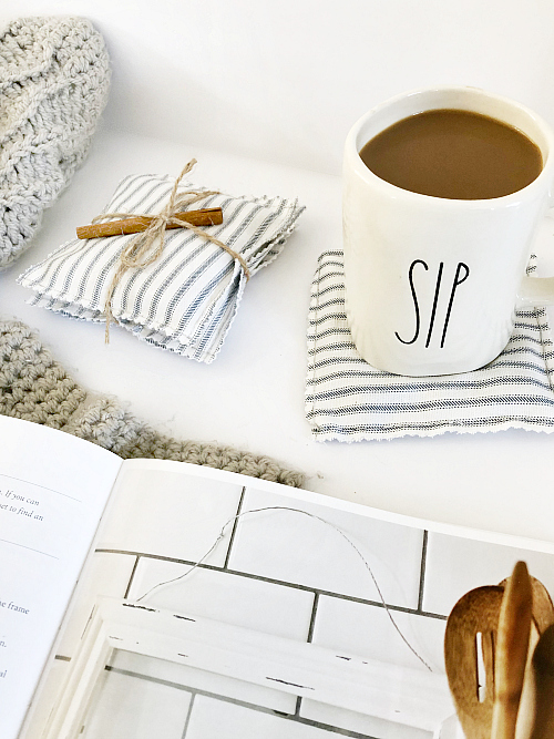 DIY Coasters tied with twine and a cinnamon stick, displayed with a mug full of coffee, and knit blanket, and a book